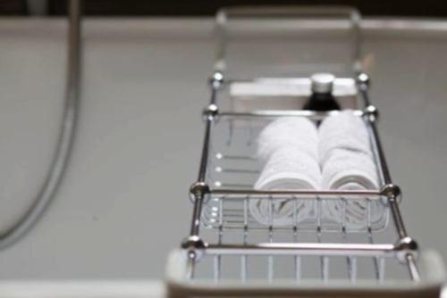 Hurley House - A chrome bathtub caddy holding two rolled white towels and a black bottle, placed over a white bathtub.