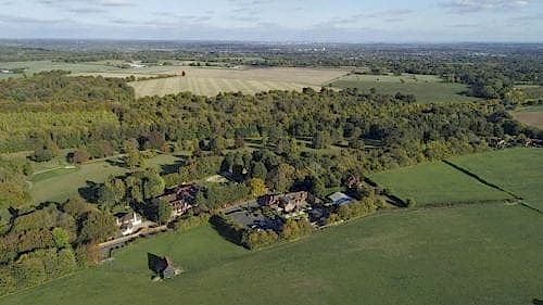 Hurley House - Aerial view of a rural landscape with clusters of houses surrounded by fields and forests. The horizon features distant patches of trees and open farmland under a sky with scattered clouds.