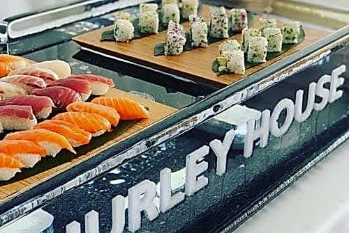 Hurley House - A display of sushi featuring assorted nigiri and rolls on wooden trays. The setting includes a glass surface with HURLEY HOUSE written in bold letters.