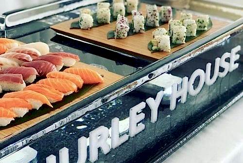 Hurley House - A display of assorted sushi on wooden boards, featuring nigiri with various fish and sushi rolls. The setup is on a reflective surface with HURLEY HOUSE in bold letters on the front.