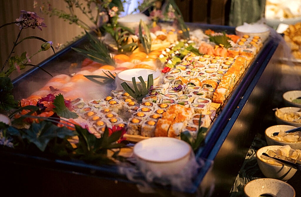 Hurley House - A large platter of assorted sushi rolls and nigiri, garnished with green leaves and flowers, is displayed on a bed of ice at a buffet in a luxury wedding venue in Berkshire, with several small bowls of dipping sauces nearby.