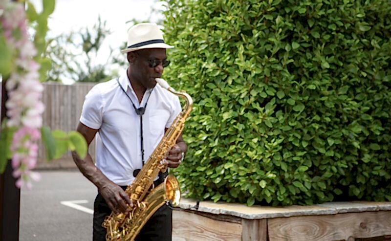 Hurley House - A man in a white shirt and hat plays a saxophone outdoors near a lush green hedge, as if setting the serene tone for a luxury wedding venue in Berkshire.